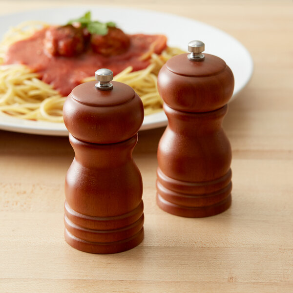 Two Acopa matte brown wooden pepper mills on a table with a plate of spaghetti.