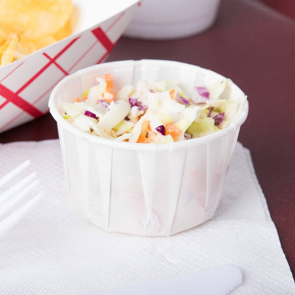 A Solo white paper souffle cup filled with coleslaw on a counter.
