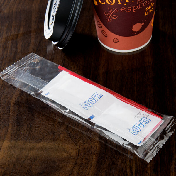 A clear plastic bag of white sugar packets next to a coffee cup.