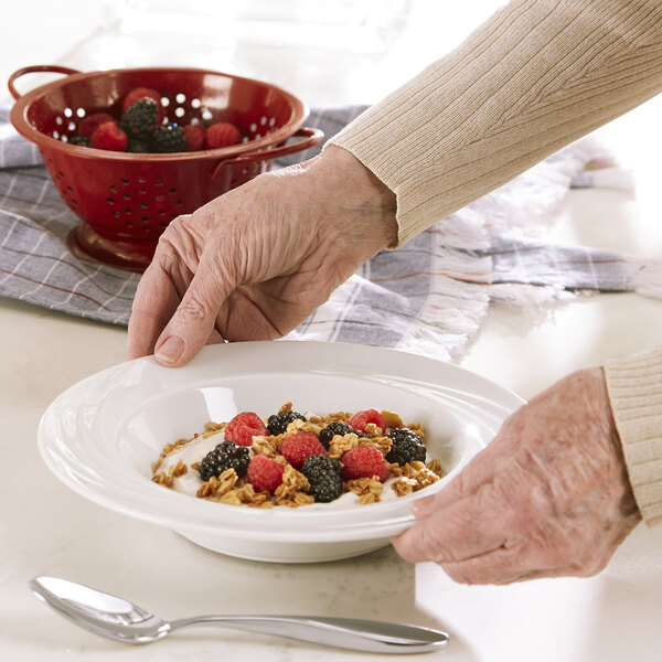 A person holding a Schonwald white porcelain bowl of cereal with berries.