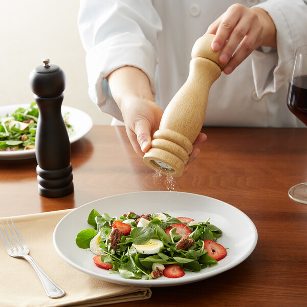 A person using an Acopa wooden pepper mill to season a salad.