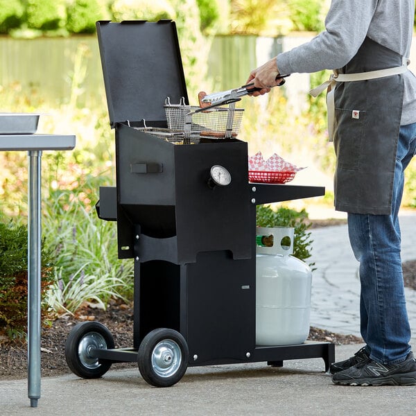 A man using a Backyard Pro liquid propane deep fryer to cook food on a table outdoors.