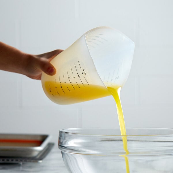A hand using a Tablecraft 3-sided silicone measuring cup to pour yellow liquid into a bowl.