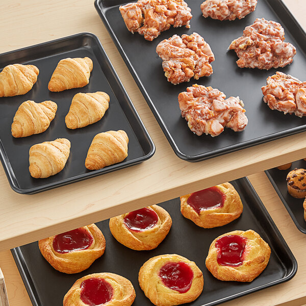 A Baker's Mark black wire rim aluminum tray of pastries on a bakery shelf.