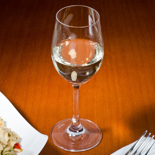 A plate of pasta with a fork next to a Stolzle port wine glass filled with white wine.