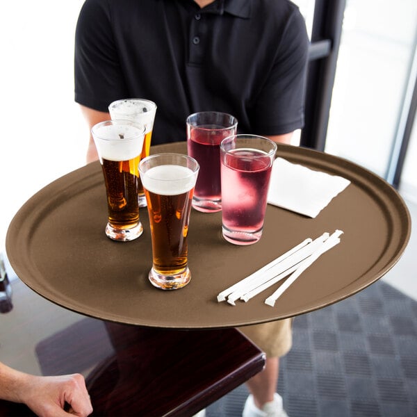 A man in a black shirt holding a Carlisle non skid oval serving tray with drinks on it.