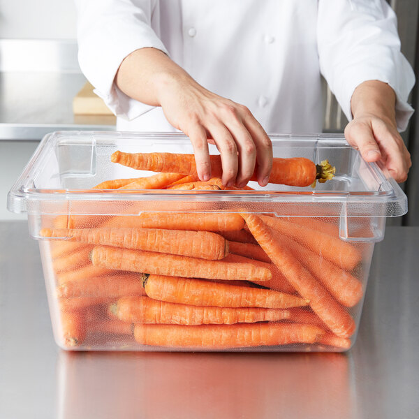 A person putting a pile of carrots in a Rubbermaid clear polycarbonate food storage container.