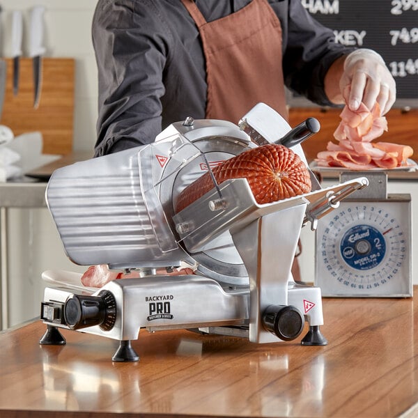 A person in an apron using a Backyard Pro meat slicer to cut meat.