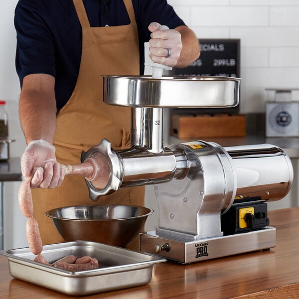A man using a Backyard Pro electric meat grinder on a counter to make sausages.
