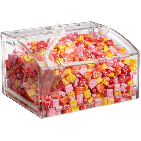 A clear plastic Rosseto bulk bin full of colorful candy with a scoop inside.