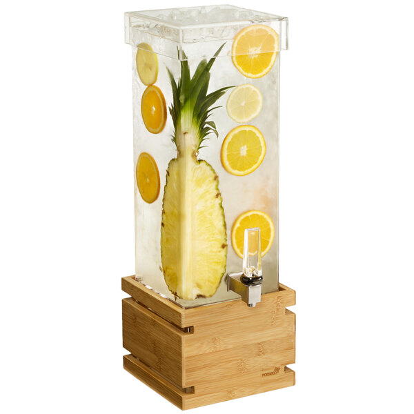 A clear plastic beverage dispenser with a bamboo base filled with pineapple and lemon slices.