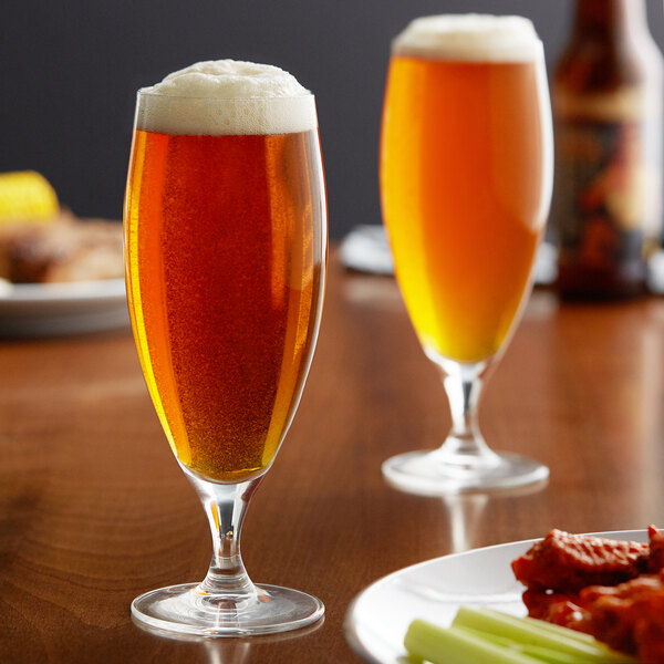 Two Reserve by Libbey stemmed pilsner glasses of beer on a table with food.