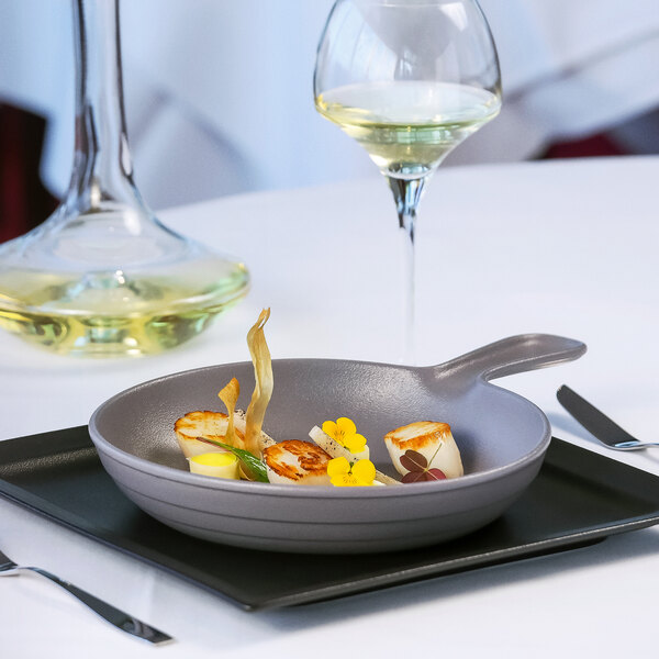 A RAK Porcelain stone gray porcelain frying pan of food on a table in a fine dining restaurant.