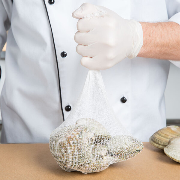 A person in white gloves holding a food grade net bag of clams.