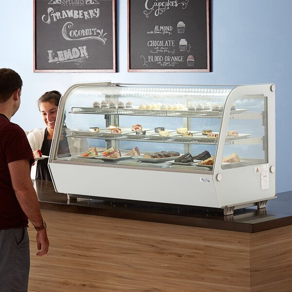 A man and woman looking at a white Avantco countertop bakery display case full of desserts.