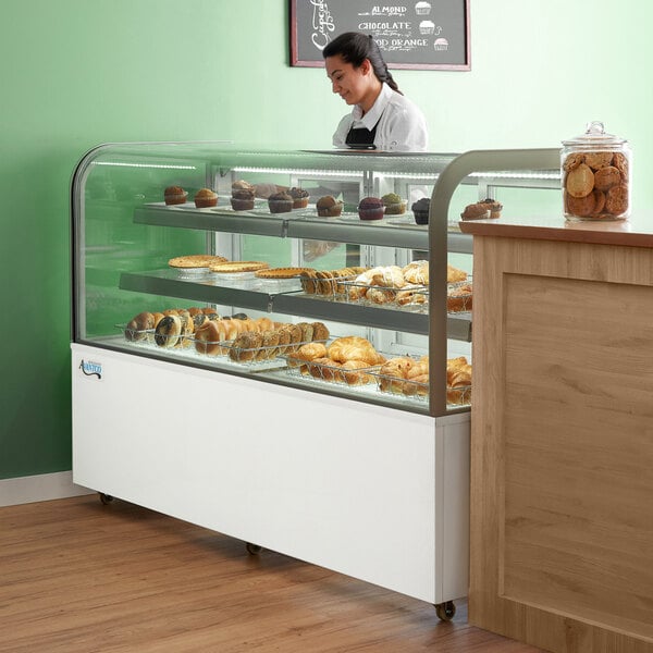 A woman in a white shirt standing behind a curved glass display case of pastries.