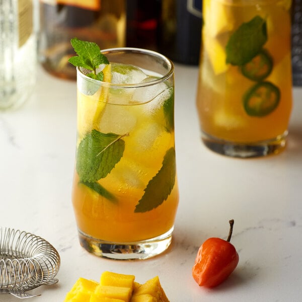A glass of orange Monin Spicy Mango drink with mint leaves and a small red pepper.