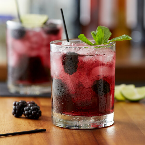 A glass of red liquid with ice and Monin Wild Blackberry syrup, garnished with berries.