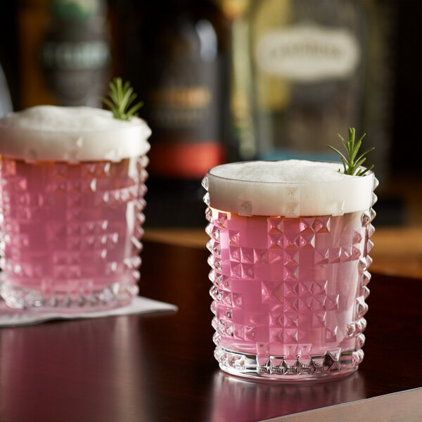 Two Nachtmann double old fashioned glasses filled with pink liquid and rosemary sprigs.