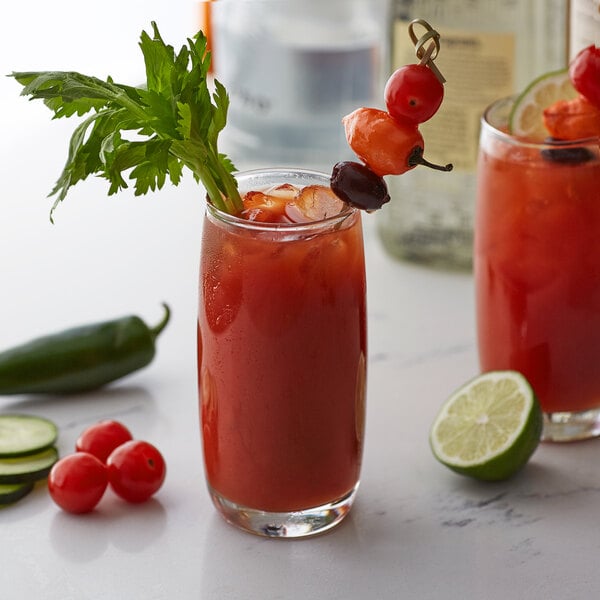 A pair of glasses of red drinks with lime and celery on the rim.
