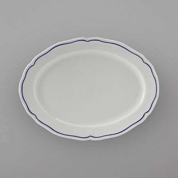 A white Tuxton china oval platter with scalloped edges and blue trim.