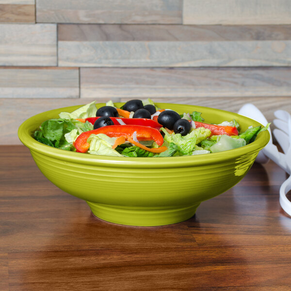 A green Fiesta pedestal serving bowl filled with salad on a table.