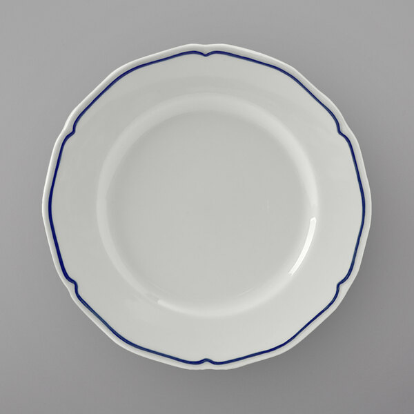 A close up of a Tuxton white china bread and butter plate with a scalloped edge and blue trim.