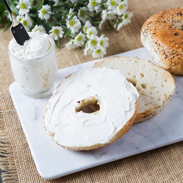 A bagel with Smithfield Amish Country cream cheese and a jar of cream cheese on a marble plate.