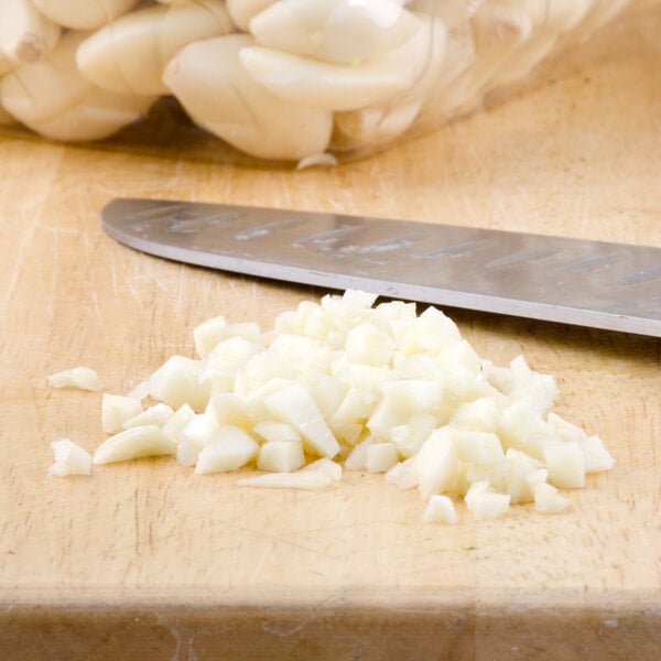 A knife next to a pile of peeled garlic on a cutting board.