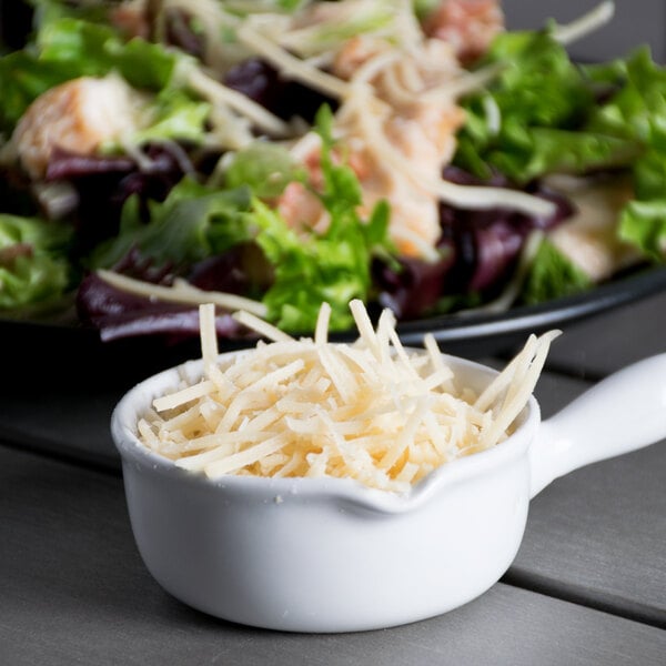 A white bowl of Marano Select shredded Parmesan cheese on a table with salad.