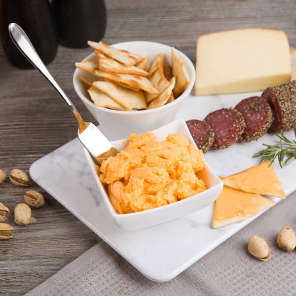 A plate of food with Kaukauna sharp yellow cheddar cheese spread, cheese, and crackers with a knife.