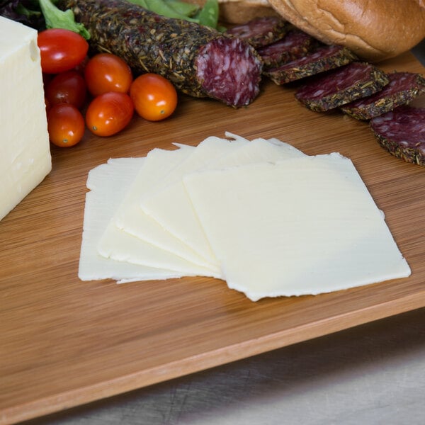 A cutting board with Land O Lakes white American cheese, bread, and vegetables.