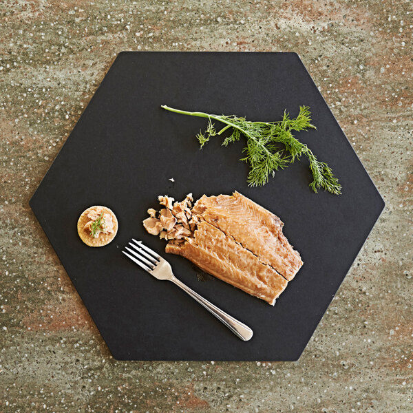 A piece of fish with a fork on a black Epicurean hexagon serving board.
