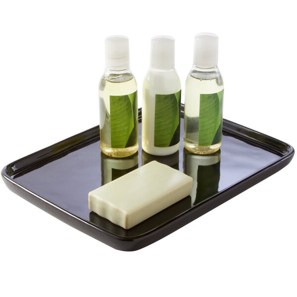 A black rectangular ceramic amenity tray holding bottles of liquid and a bar of soap.