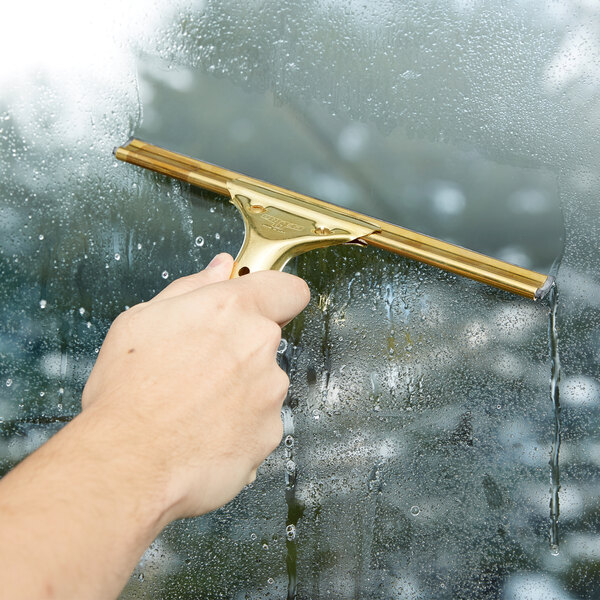A person using the Unger GoldenClip window squeegee with a brass handle to clean a window.