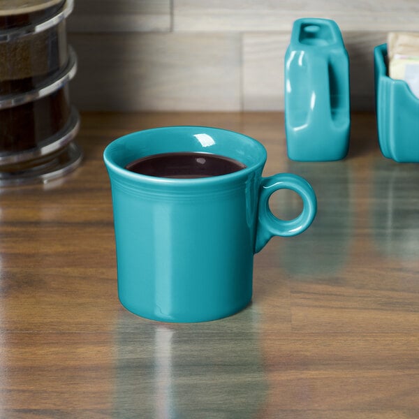 A turquoise Fiesta china mug with a handle full of a drink on a wood surface.