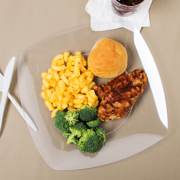 A Fineline clear plastic plate with a chicken breast, broccoli, and mashed potatoes on a table.