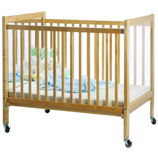 A wooden Whitney Brothers I-See-Me infant crib with wheels and a blue blanket on it, with a white stuffed animal on it.