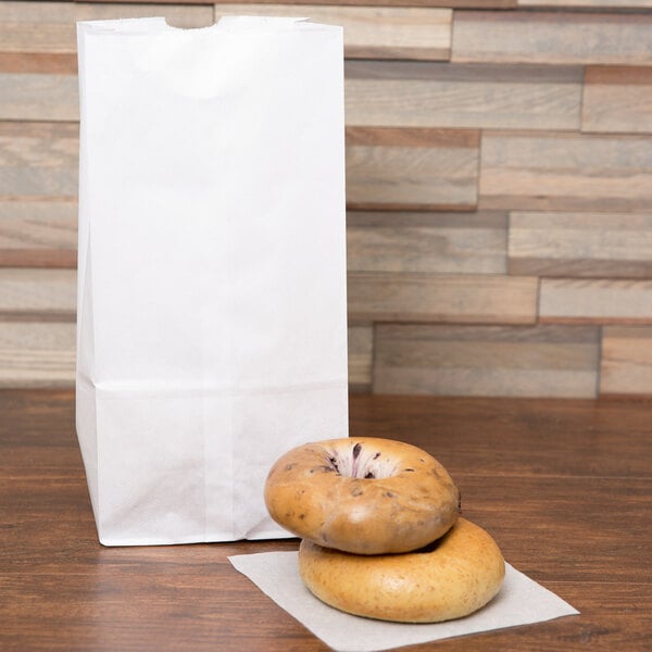 A bagel with a hole in the middle on a white napkin next to a white paper bag.