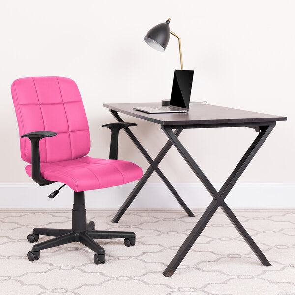 A Flash Furniture pink mid-back office chair with armrests next to a black desk with a laptop on it.