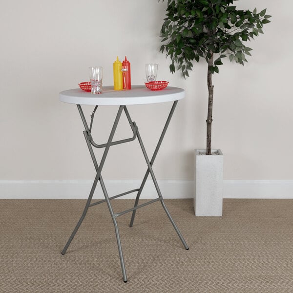 A Flash Furniture round white plastic folding table with a plant on it in front of a tree.