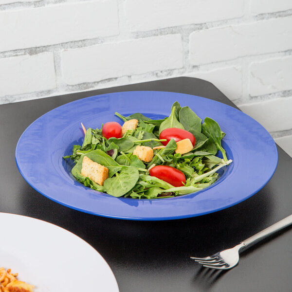 A Carlisle Ocean Blue melamine chef salad bowl with a salad and a silver fork on a table.