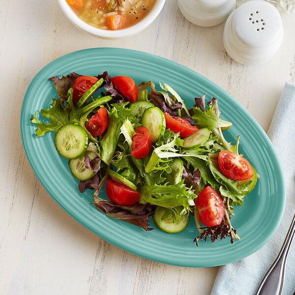 A Tuxton oval china platter with a salad of tomatoes, cucumbers, and lettuce.