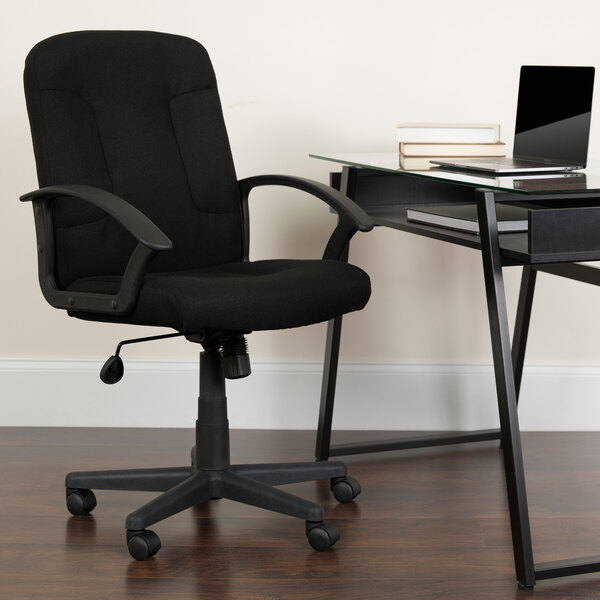 A black Flash Furniture office chair with armrests at a glass desk with a laptop.