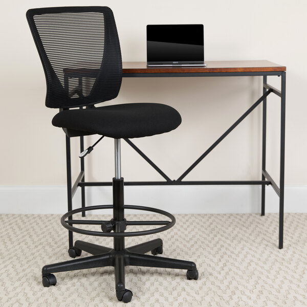 A black Flash Furniture mesh drafting chair at a desk with a laptop.