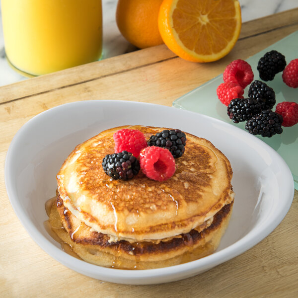 A stack of pancakes with berries on top served on a Carlisle Griege Melamine Pasta Plate with a glass of orange juice on the side.