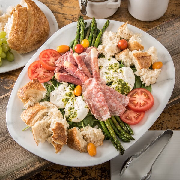 A Carlisle marble melamine oblong platter with asparagus, tomatoes, and bread on a table.