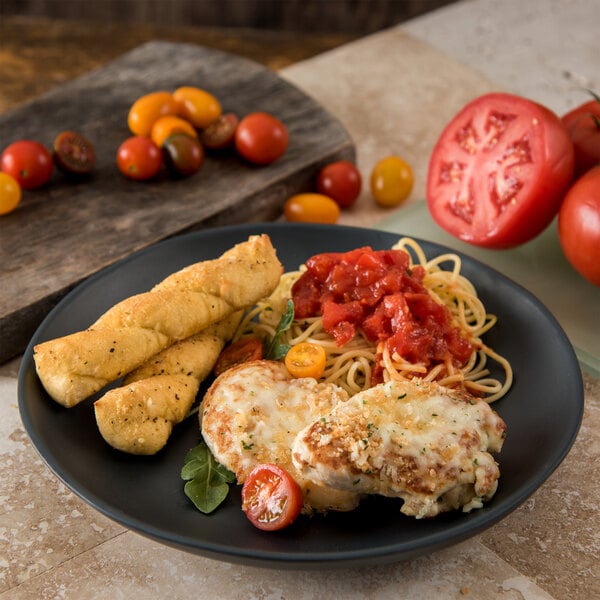 A Carlisle slate melamine dinner plate with food including a tomato and breadsticks on a table.