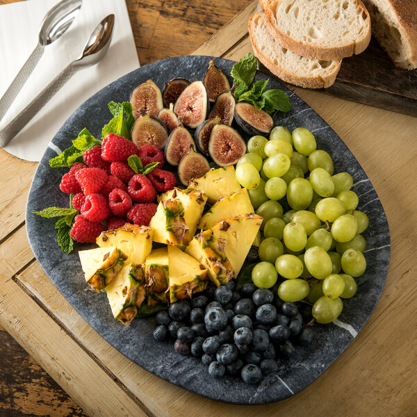 A Carlisle Soapstone Melamine oblong platter with fruit and bread on a table.