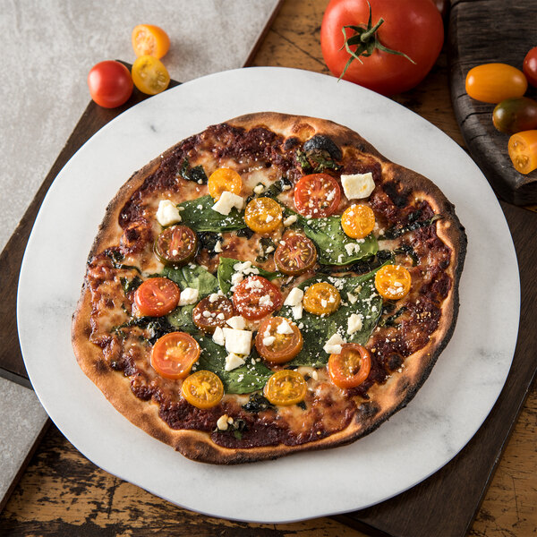 A pizza with tomatoes, cheese, and spinach on a Carlisle white melamine plate.